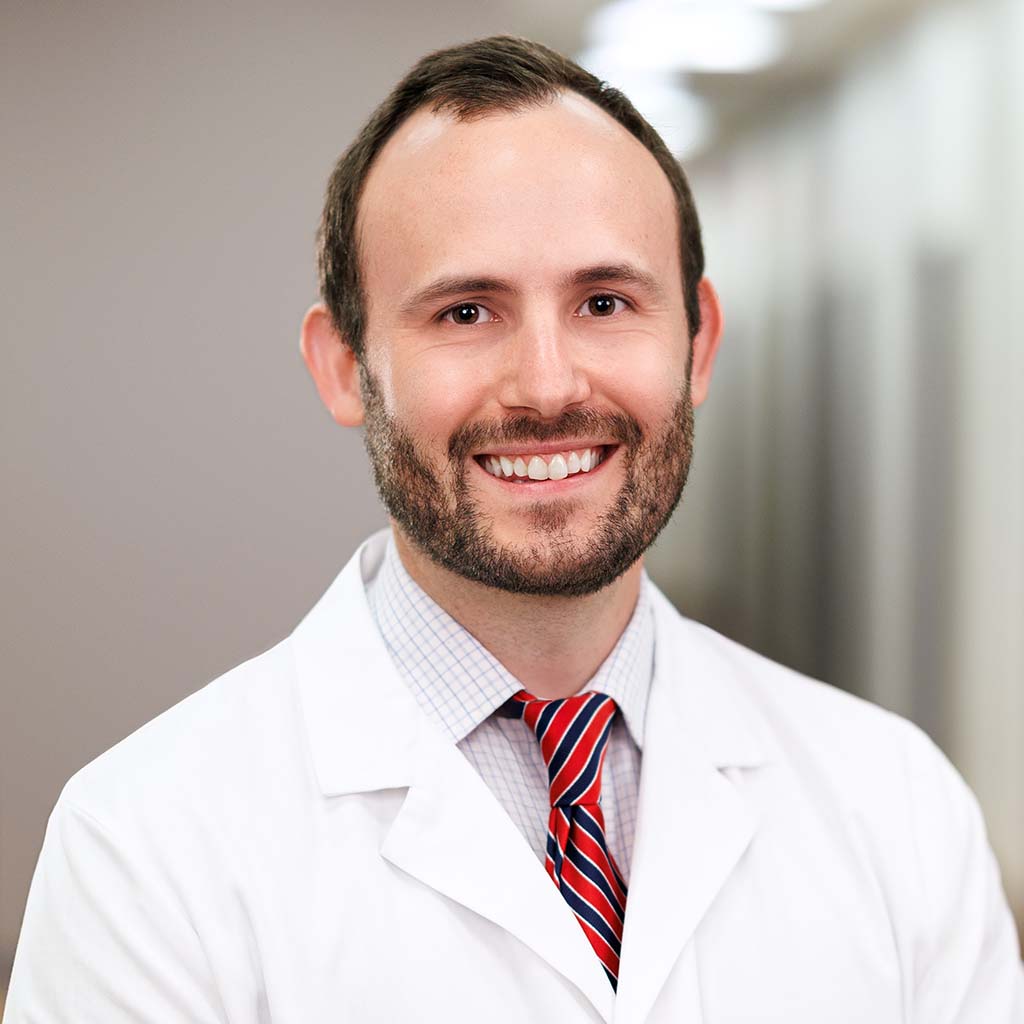 Dr. Stevens smiling and wearing his white coat in the clinic hallway.
