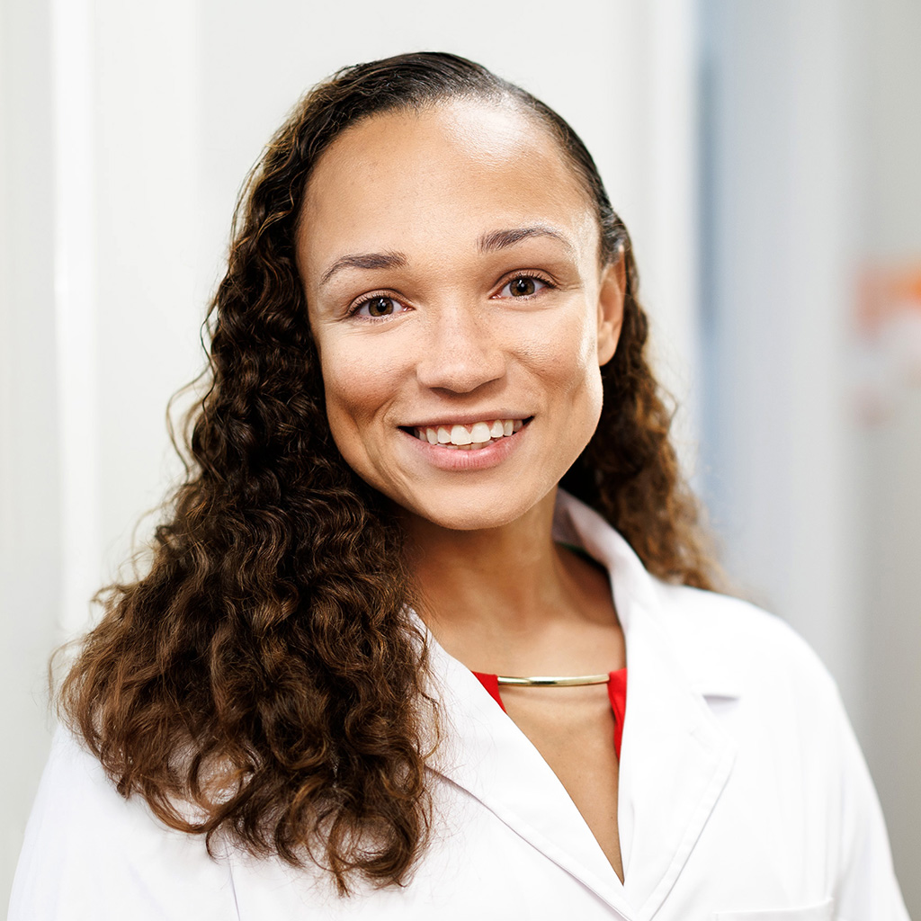 Dr. Satchell smiling and wearing her white coat in the clinic hallway.