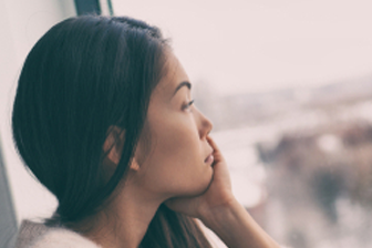 Asian woman looks out dreary window